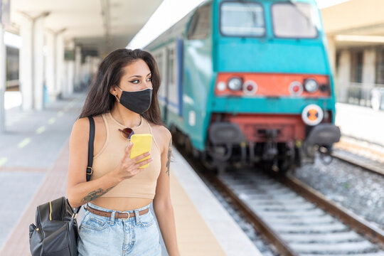 Young woman wearing face mask looking away while using mobile phone standing at station