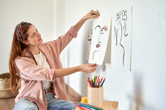 Female artist pasting charcoal drawing on wall in living room