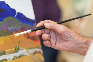 Man's hand holding paintbrush with painting in background