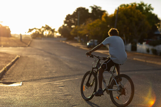 teenager riding bike with no helmet on quiet evening street