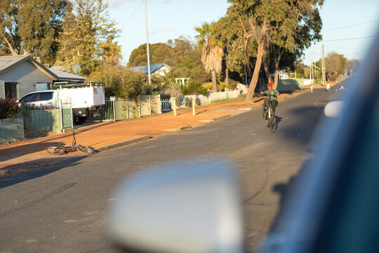 view of street with blurred car in foreground and boy doing wheelie on bike