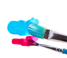 two brushes wide and narrow make strokes of dark red and blue paints on a white background.