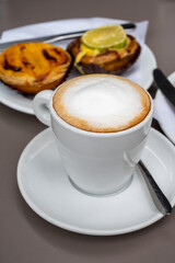 Cup of cappuccino coffee served with traditional dessert pastry in Portugal, nata eggs cream cakes with fruits
