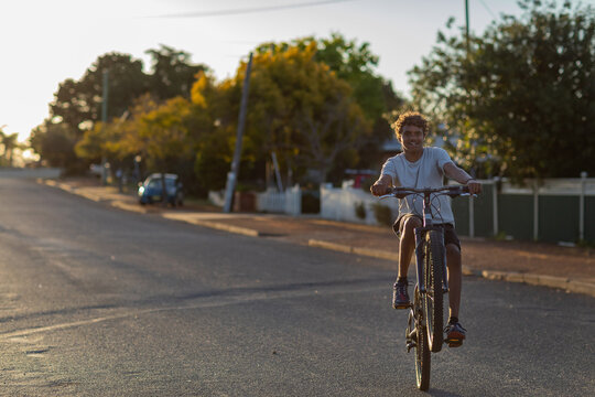 adolescent boy riding bicycle on quiet street with no helmet