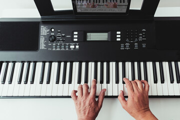 Top view of a man's hands on a piano keyboard next to a tablet with a piano lesson app. Concept of online music lessons