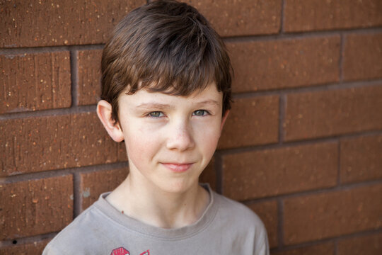 Portrait of a nine year old boy standing against brick wall