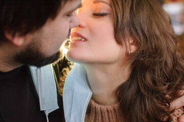 Young romantic loving couple wearing a protective face mask and staring at each other's eyes, St. Valentine's day during pandemic and quarantine.
