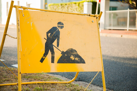 Yellow digging road work sign near construction site on footpath