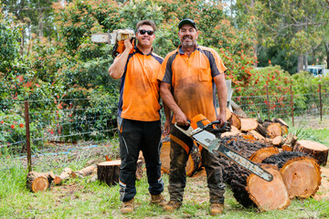 Portrait of two happy aussie blokes with chainsaws - lumberjack tree felling services