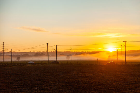 Sunrise over misty paddocks and busy road with morning rush traffic and power poles