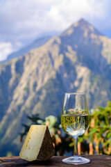 Glass of swiss or savoy dry white wine and tomme cheese with Alpine mountains peaks on background