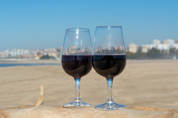 Tasting of different fortified dessert ruby, tawny port wines in glasses on sandy beach with view on waves of Atlantic ocean near Vila Nova de Gaia and city of Porto, Portugal