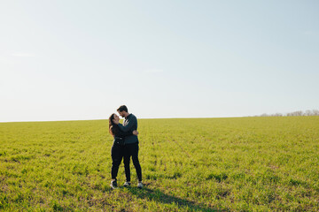 Young happy couple hugging on a green meadow with blue sky on the background. Copy space.