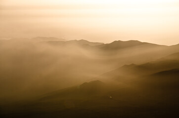 Sun beams passing through dawn mist with silhouettes of mountains, ridges and peaks, Tenerife, Canarian Islands