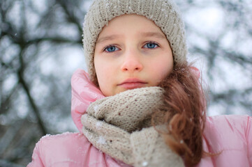 Sad child girl in warm knitted winter clothes spent time outdoors and got frozen.