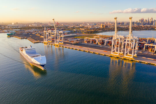 Aerial view of a cargo ship cruising past large gantry cranes on a dock