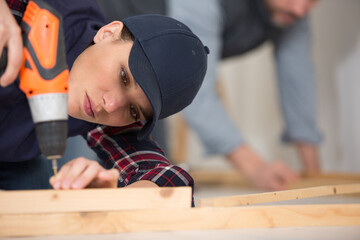 woman drills a screw in a wooden construction
