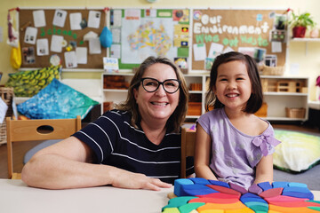 Happy multicultural teacher and child with wooden blocks puzzles in kindergarten