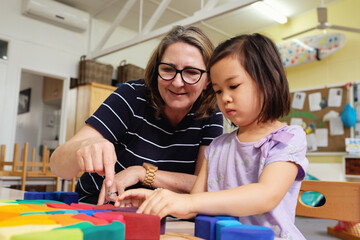 Multicultural teacher and child playing wooden blocks puzzles in kindergarten