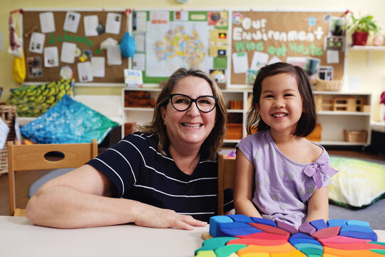 Happy multicultural teacher and child with wooden blocks puzzles in kindergarten