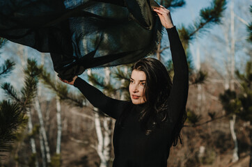 Portrait of a woman waving a forest green scarf caught in motion, in a woods setting background	