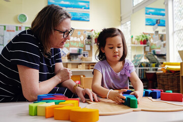 Multicultural teacher and child playing wooden blocks puzzles in kindergarten