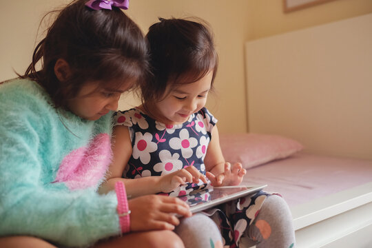 Multicultural kids using tablet in bedroom