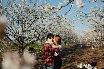 Passionate couple hugging near blossoming cherry trees. They walking in spring garden.