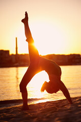 Silhouette of a young blonde woman practicing yoga at sunset near the river.