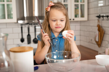 seriously intentional nfocused little girl is about to break an egg with a knife. cooking pancakes.