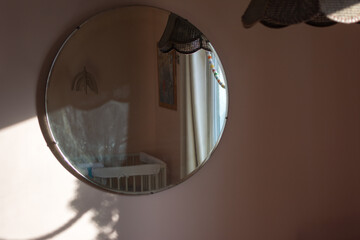 Baby nursery reflected in round vintage mirror; retro pendant lamp, crib, mobile, decor