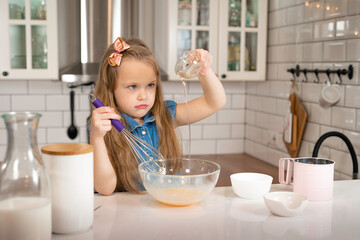 kid is cooking. little girl pouring butter into a bowl of eggs, holding a whisk with the other hand.