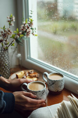 Obraz na płótnie Canvas hand holding a cup of coffee and cookies near rainy window