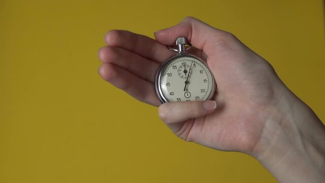 A woman's hand holds an analog stopwatch on a yellow chrome screen. The time starts with the old chronometer, the person presses the Start button in the sports concept. The concept of time management.
