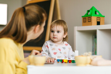Early childhood learning. Mother and child play with wooden beads and cups, teaching colors and developing fine motor skills