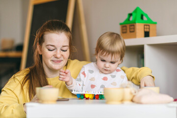 Naklejka premium Early childhood learning. Mother and child play with wooden beads and cups, teaching colors and developing fine motor skills