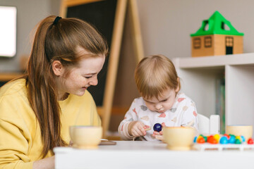 Fototapeta premium Early childhood learning. Mother and child play with wooden beads and cups, teaching colors and developing fine motor skills