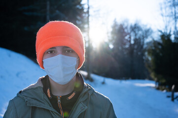 Fototapeta na wymiar Portrait of a caucasian boy wearing a mask to protect himself from the coronavirus. After the closure for the pandemic is over, he is taking a trip in the snow. Concept of relaxation in nature.