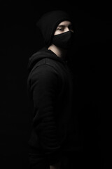 young man with black winter knit cap and face mask standing in front of black background