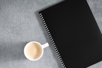 Gray office desk. Black notebook and coffee cup on gray desk background. Flat lay, top view, copy space