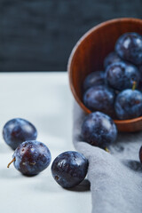 Ripe plums in a bowl with gray tablecloth on white table