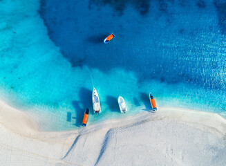 Aerial view of the yachts and fishing boats on tropical sea coast with white sandy beach at sunset in summer. Zanzibar, Africa. Colorful landscape with boats, transparent blue water. Top view. Travel - obrazy, fototapety, plakaty