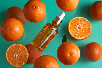 A bottle with aromatic essential tangerine oil and tangerines on a glass green  background.