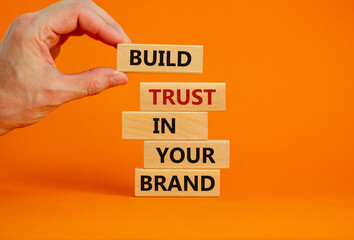 Success business process symbol. Wood blocks stacking as step stair on orange background, copy space. Businessman hand. Words 'build trust in your brand'. Business and trust brand concept.