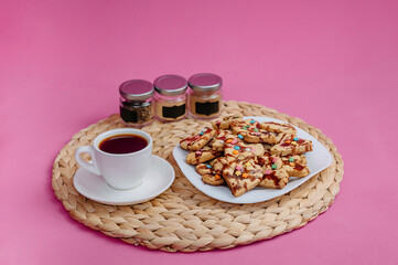Cup of coffee, homemade cookies and kitchen utensils on a pink background
