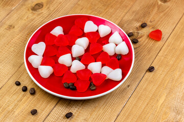 red candies in a plate in the shape of a heart on a wooden background. Valentine's Day. Place for...