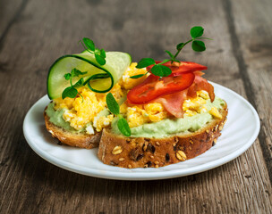 healthy snack, sandwiches with cereal bread, avocado cream, scrambled eggs and cucumber on a wooden table