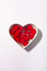 White heart shaped bowl with red rose petals on the water surface