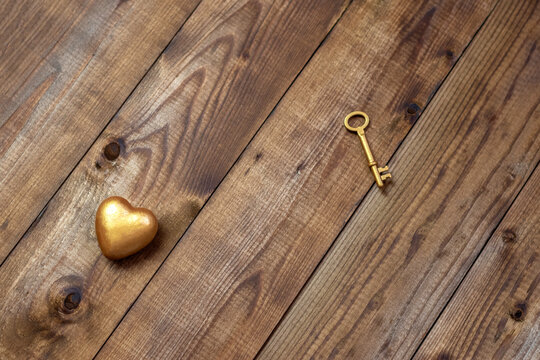 Top view shot of gold heart and key on wood background with copy space