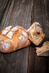 Country bread with floured crust with pieces on a barn wood board on white background